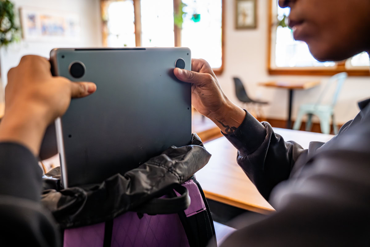 A woman in a coffee shop removes her laptop from the ULA Packrat