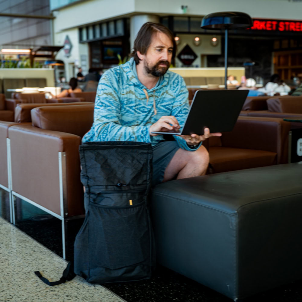Urban traveler works on laptop in airport, with the ULA Ultra Node open next to him