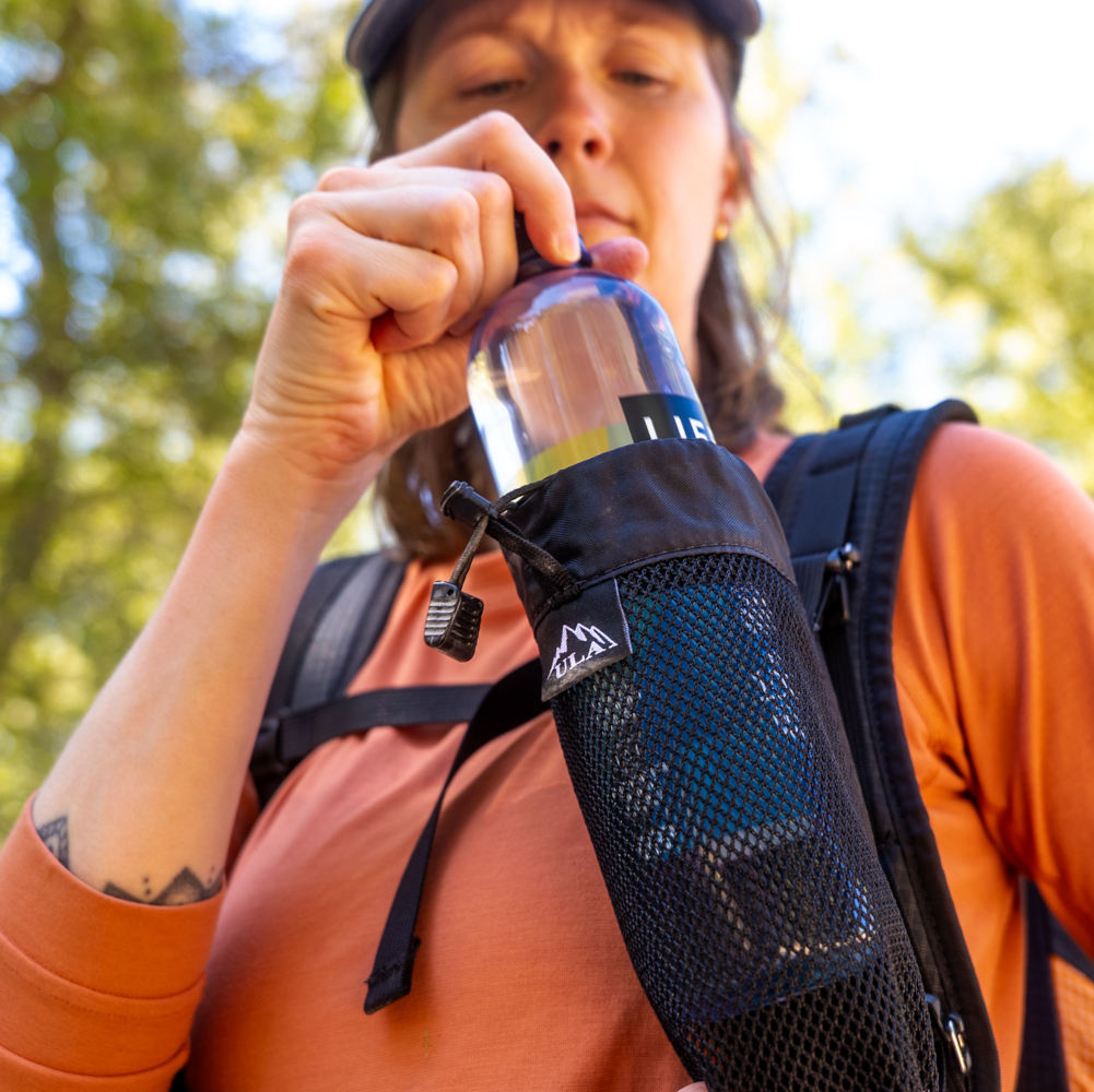 Hiker removes water bottle from a ULA Flow attached to her shoulder strap.